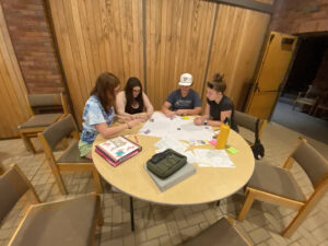 Four students sitting at a circle table making their map of the neighborhood after their prayer walk. 